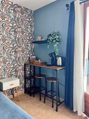 A small, cozy room with a patterned wallpaper, a desk with a kettle, and a potted plant. - Bleuet Suite in Peyriac-de-Mer with a terrace, private parking, and air conditioning🦋 (Peyriac-de-Mer)