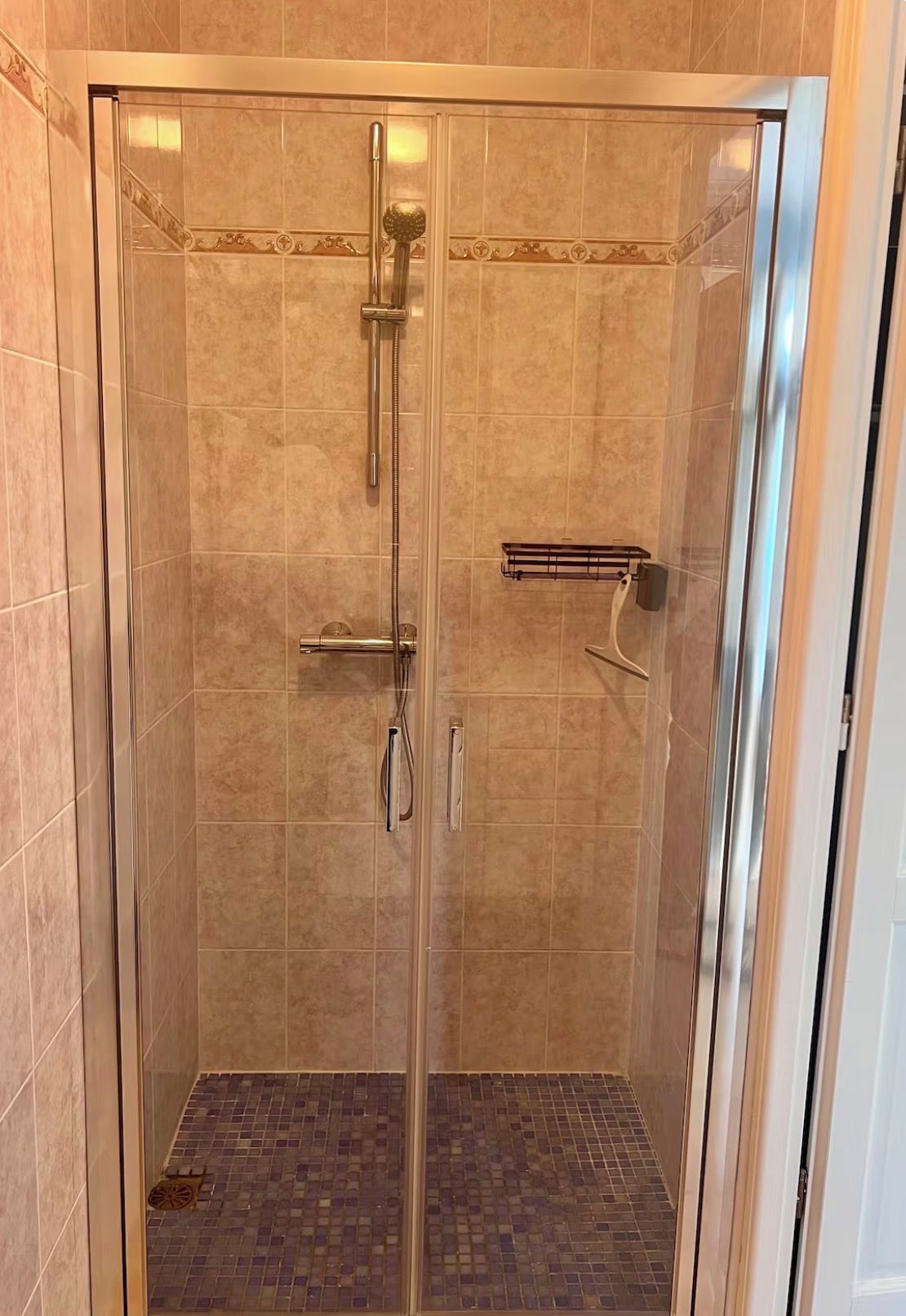 Un box de ducha con paredes de vidrio, piso de baldosas, ducha de mano y barra para toallas.