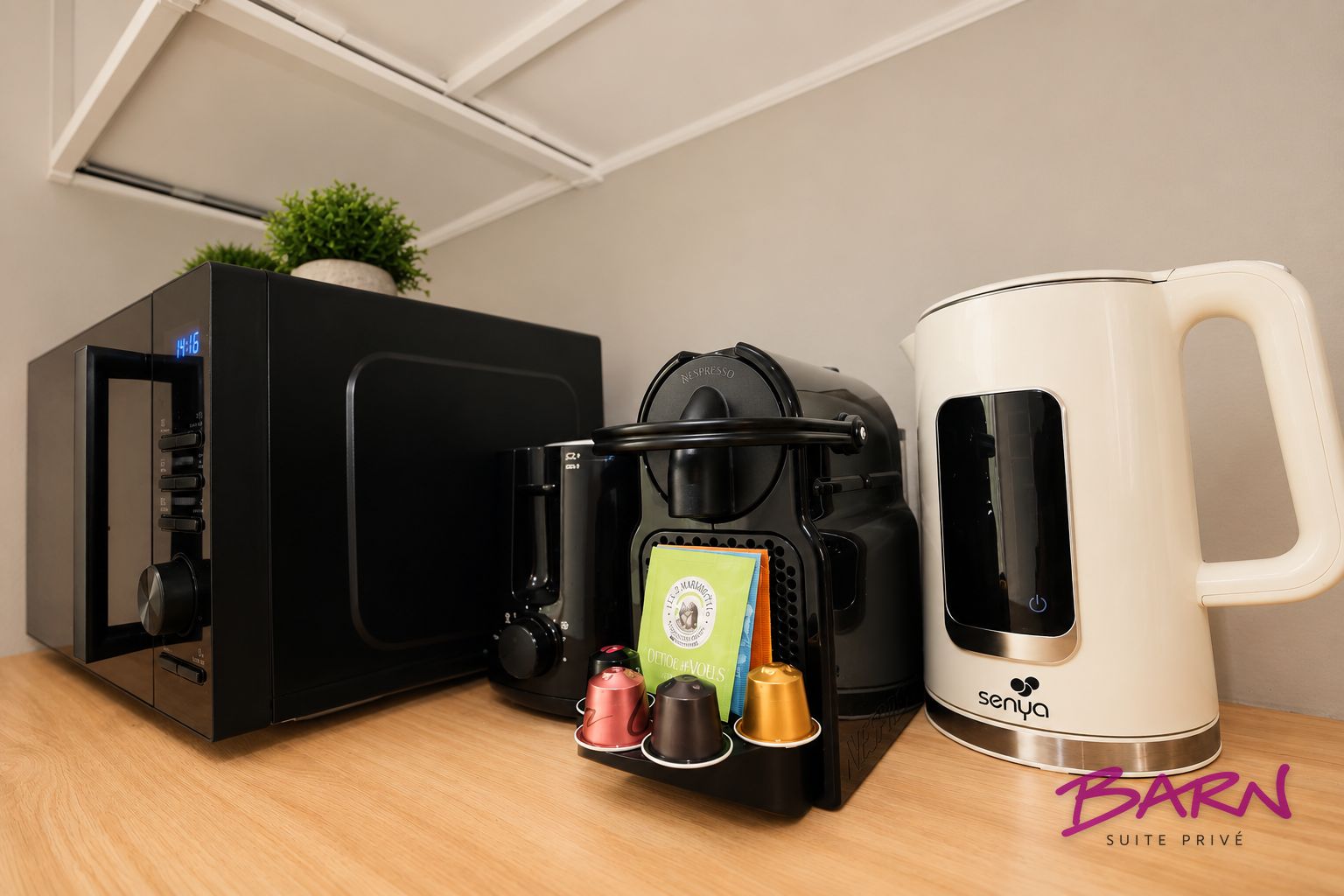 Een koffieapparaat, een Nespresso-capsuledispenser en een witte koffiekan op een houten oppervlak.