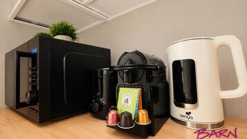 Een koffieapparaat, een Nespresso-capsuledispenser en een witte koffiekan op een houten oppervlak.