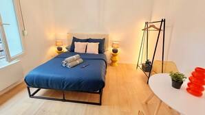 A modern bedroom with a bed, bedside lamps, a hanging light fixture, a small table with a plant, and a chair. - Le BARN -> a stylish urban retreat ❤️ (Le Havre)