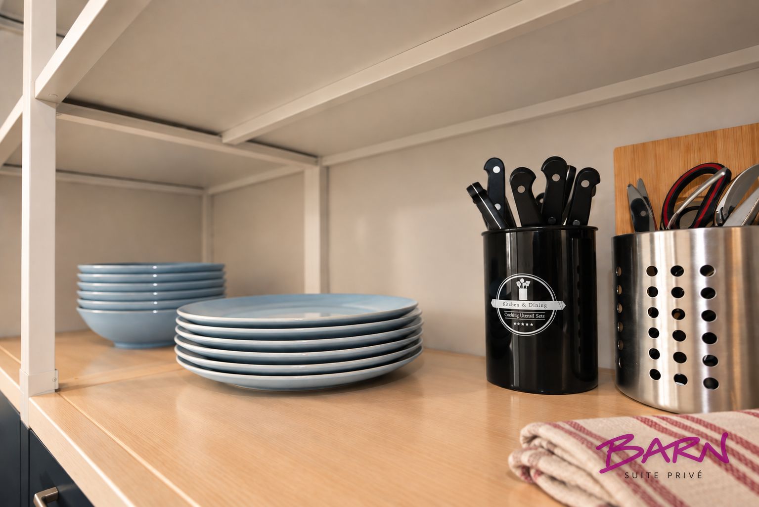 Una repisa de cocina con platos azules apilados, un portavasos negro con cuchillos y un agarrador de olla de acero inoxidable.