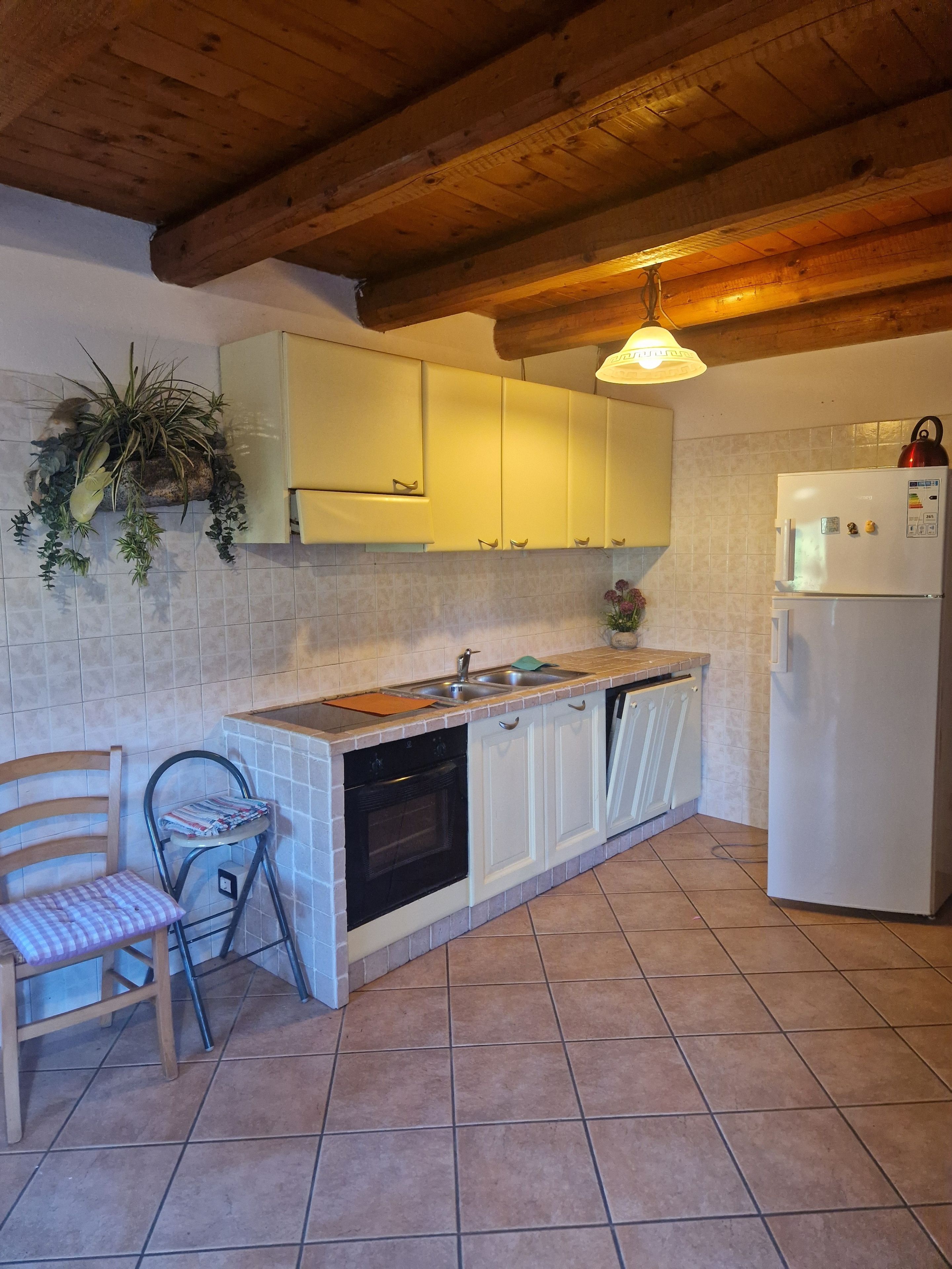 Eine Küche mit weißen Schränken, einer gefliesten Spritzschutzwand, einer Holzbalkendecke und einem weißen Kühlschrank.