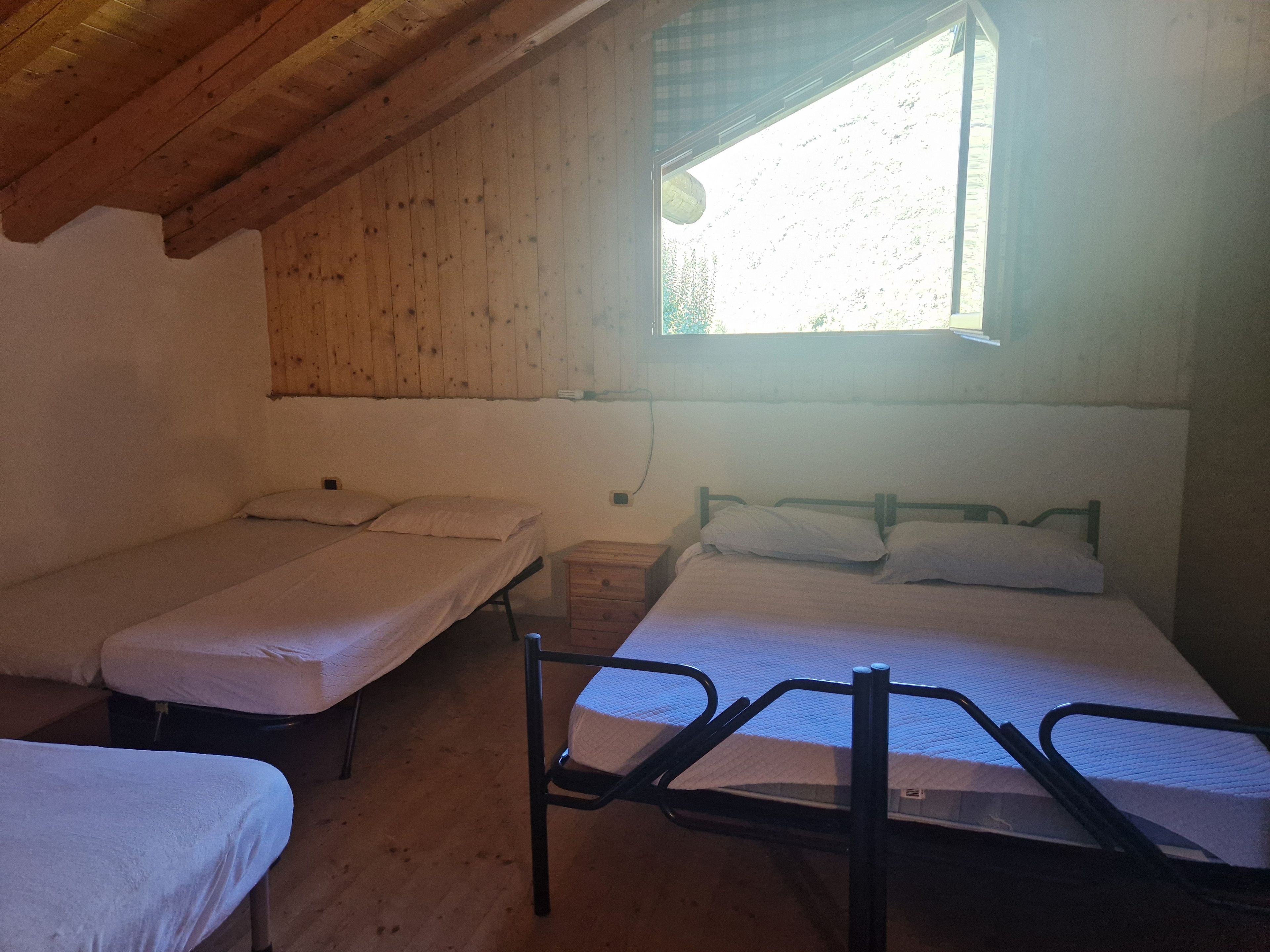 A room with two single beds and a larger bed, wooden walls, a window with a view, and a wooden ceiling.