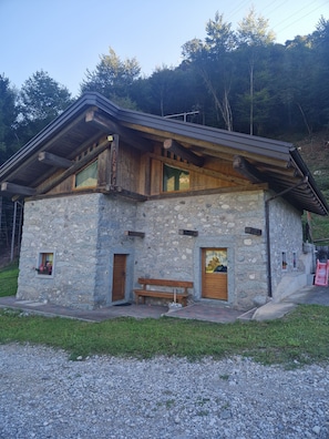 A stone building with a wooden bench, wooden doors, and a window with a green curtain.