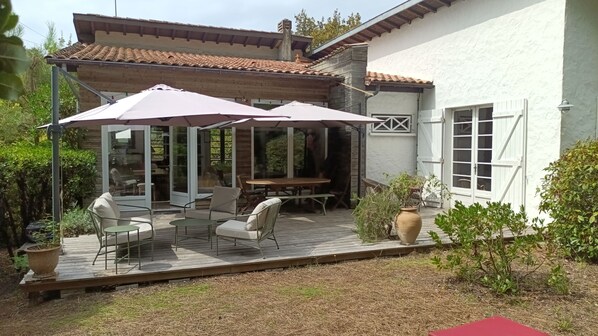 Eine Terrasse mit Gartenmöbeln, einem überdachten Sitzbereich und Blick auf das Haus.