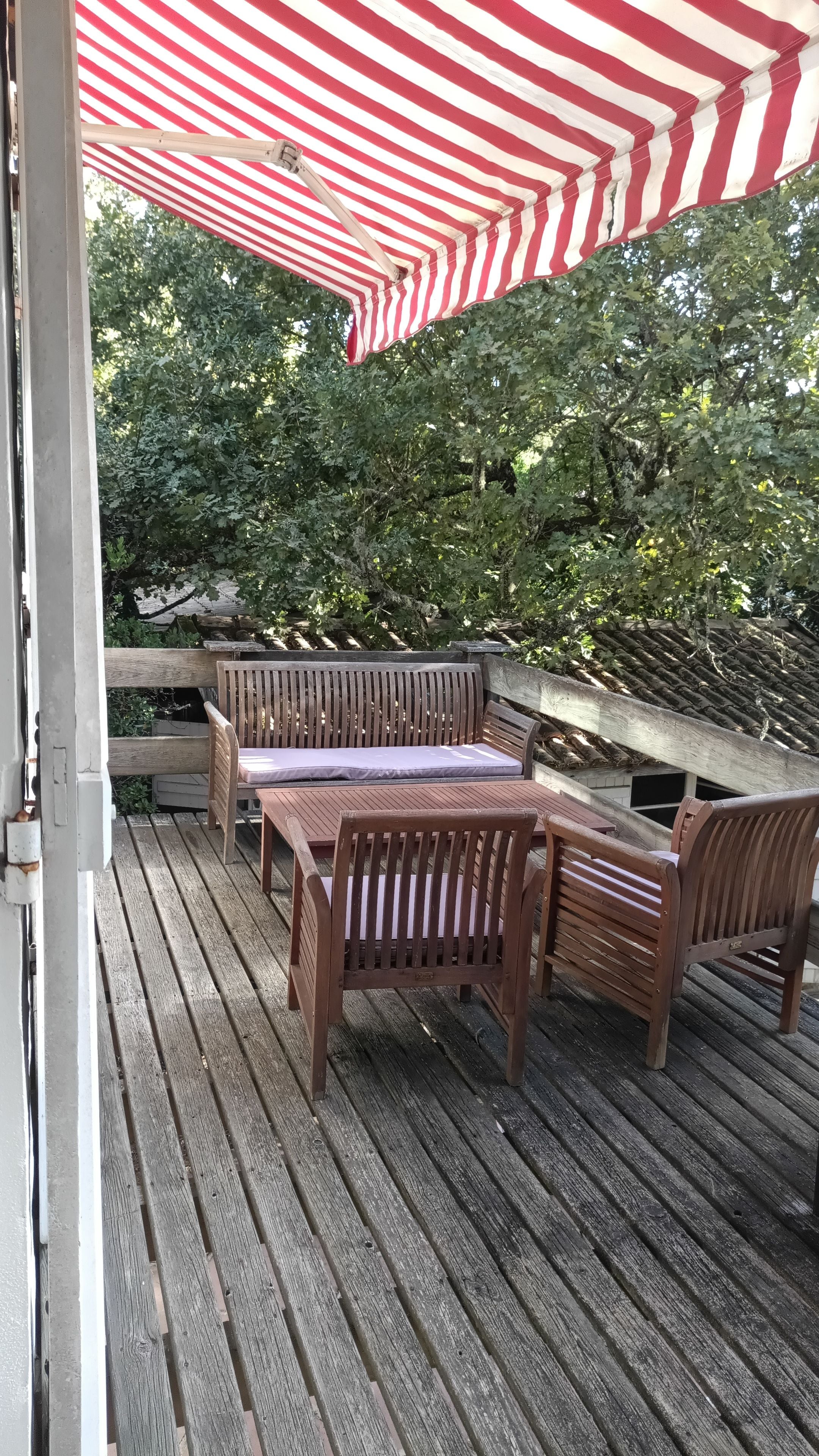 Eine Holzterrasse mit Picknicktisch und Bänken, einem Sonnenschirm und Bäumen im Hintergrund.