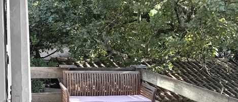 A wooden deck with a picnic table and benches, an umbrella, and a backdrop of trees.