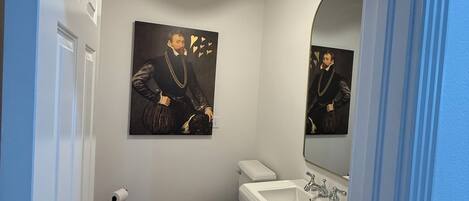 Un baño con inodoro, lavamanos y un cuadro en la pared.