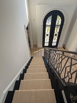 Una escalera con barandilla, escalones alfombrados y una puerta con un panel de vidrio decorativo.