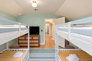 A room with bunk beds, a television, a wooden dresser, and a door leading to another room. - 4BR Emerald Coast Escape | Pool, Hot Tub & Theater (Fort Walton Beach)