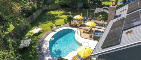 Un jardin à l’arrière d’une maison, avec une piscine, des meubles de jardin et des panneaux solaires sur le toit.