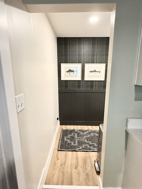 A narrow hallway with a wooden floor, a black and white rug, and two framed pictures on the wall.