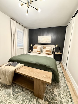 A bedroom with a bed, bedside tables, a bench, a rug, and a ceiling light fixture.