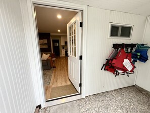 Une porte donne sur un espace de vie avec une cuisine à l’arrière-plan, une petite fenêtre et un porte-gilets de sauvetage fixé au mur.