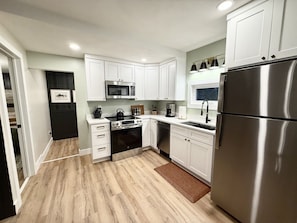 A modern kitchen with white cabinets, stainless steel appliances, and a wooden floor.