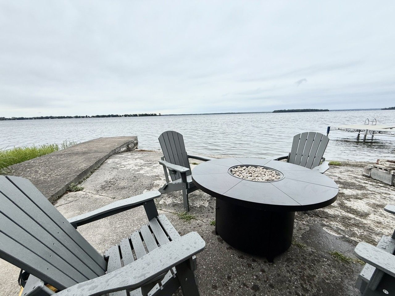 A waterfront outdoor seating area with a round table and four Adirondack chairs.