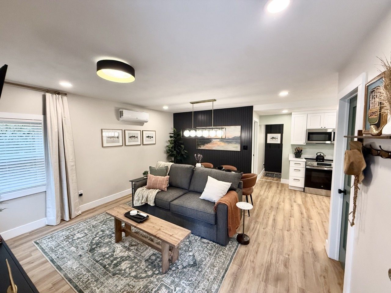 A modern living room with a sofa, coffee table, and a dining area. There is a kitchen in the background with cabinets and appliances.