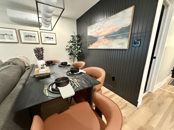 Un comedor con una mesa de madera oscura preparada para cuatro personas, rodeada de sillas anaranjadas.