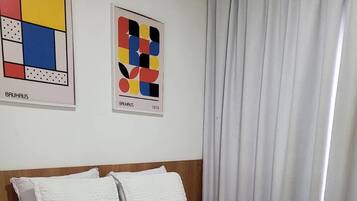 Una cama bien hecha con ropa blanca y dos almohadas, una mesita de noche con una lámpara y dos obras de arte abstracto en la pared.