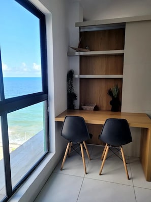 Una habitación con un ventanal grande con vistas al mar, un escritorio de madera con dos sillas negras y estanterías empotradas.