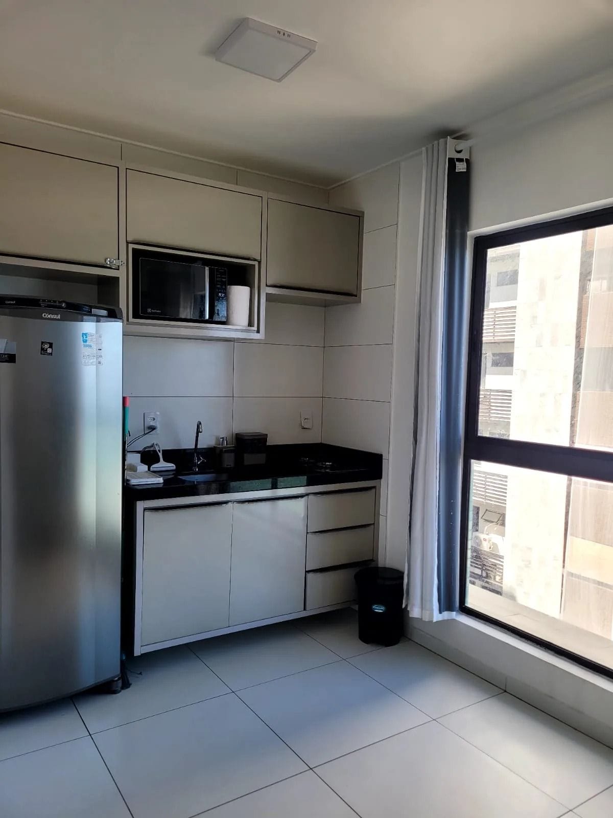 A compact kitchen with a refrigerator, microwave, and a window with a view of buildings.