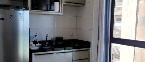 A compact kitchen with a refrigerator, microwave, and a window with a view of buildings.
