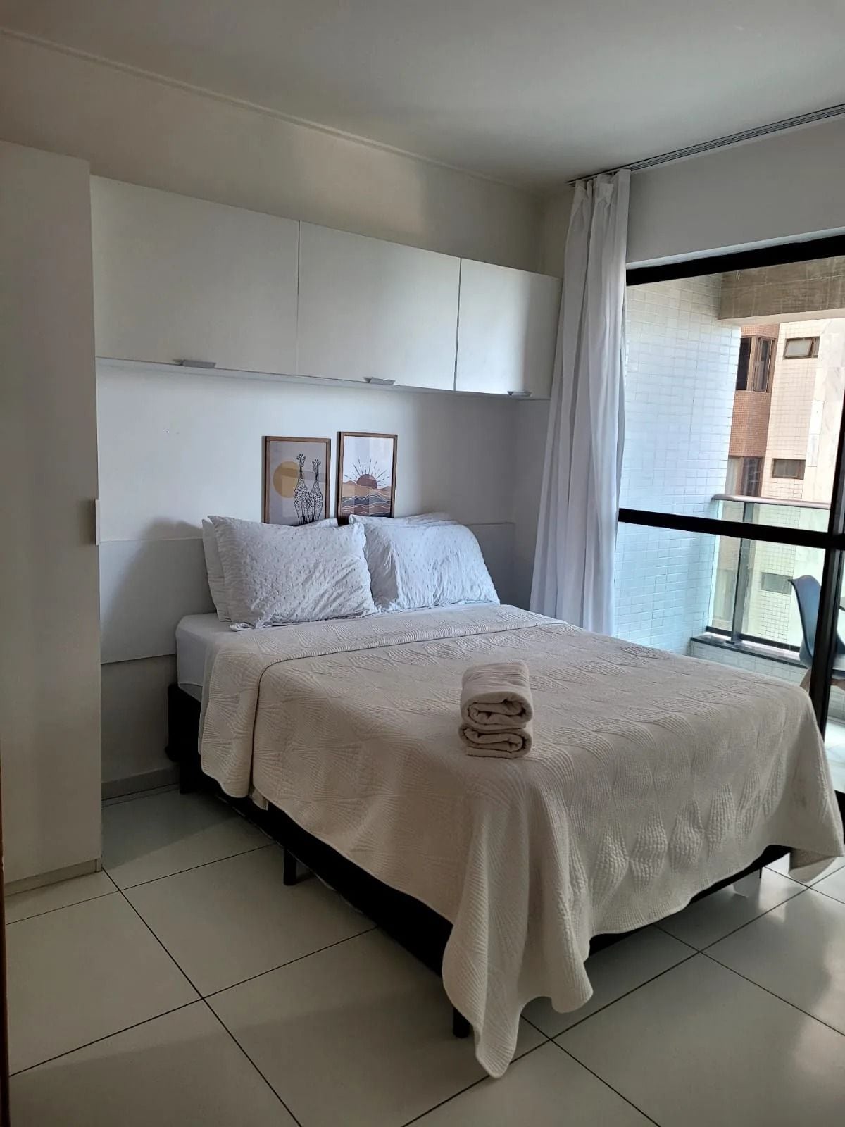 Un dormitorio con cama, una ventana con cortinas y vistas a edificios.