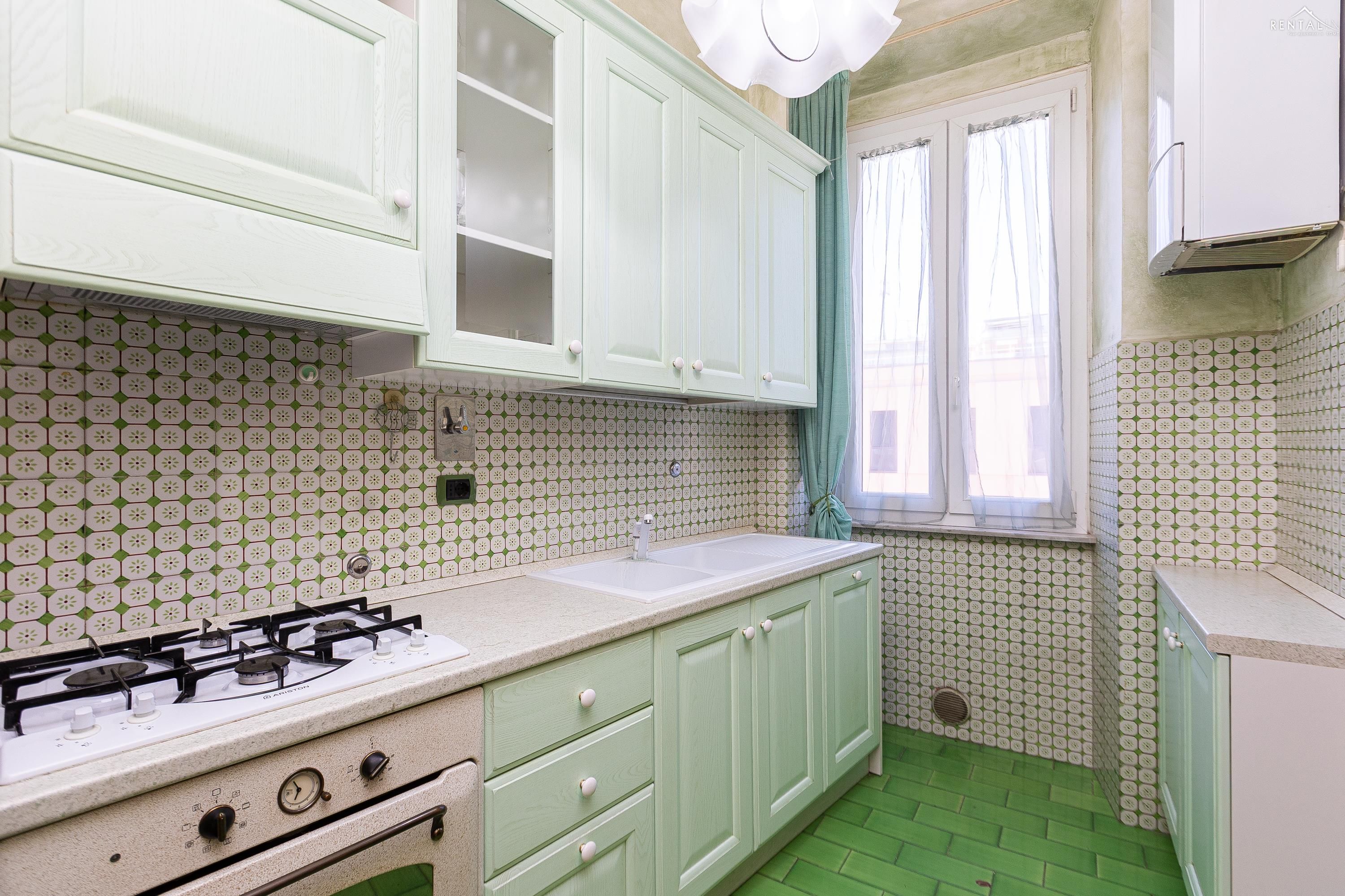 Een keuken met groene kastjes, een gasfornuis en een tegelachtergrond met een patroon.