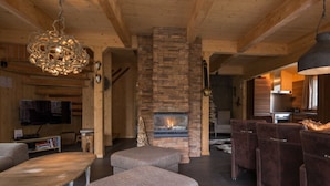 A cozy living room with a stone fireplace, wooden beams, and a television. - Cabin in Turrach With Sauna and Wi-fi (Stadl-Predlitz)