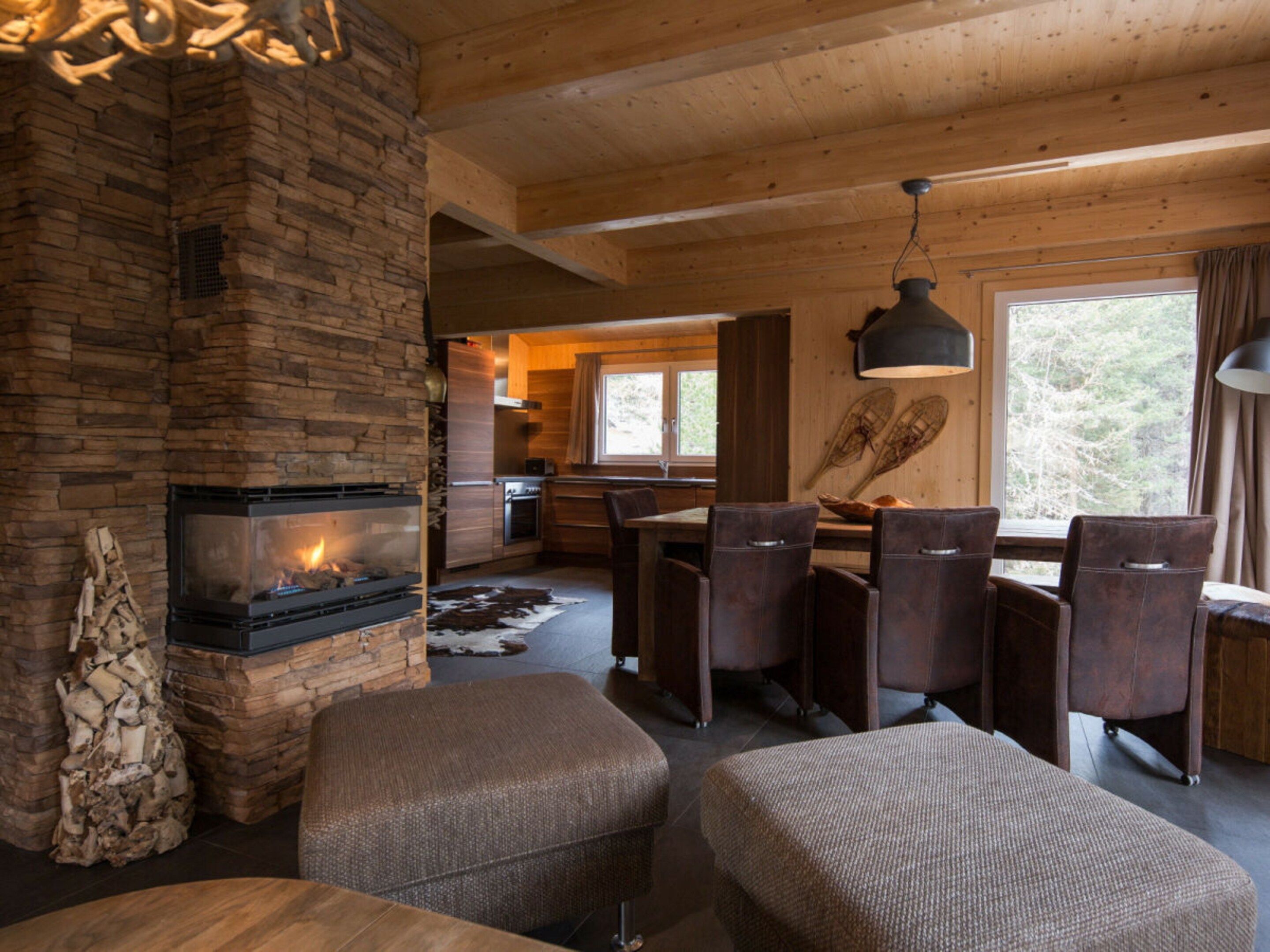 Un salon chaleureux avec une cheminée en pierre, un plafond en bois et un coin repas doté de fauteuils en cuir.