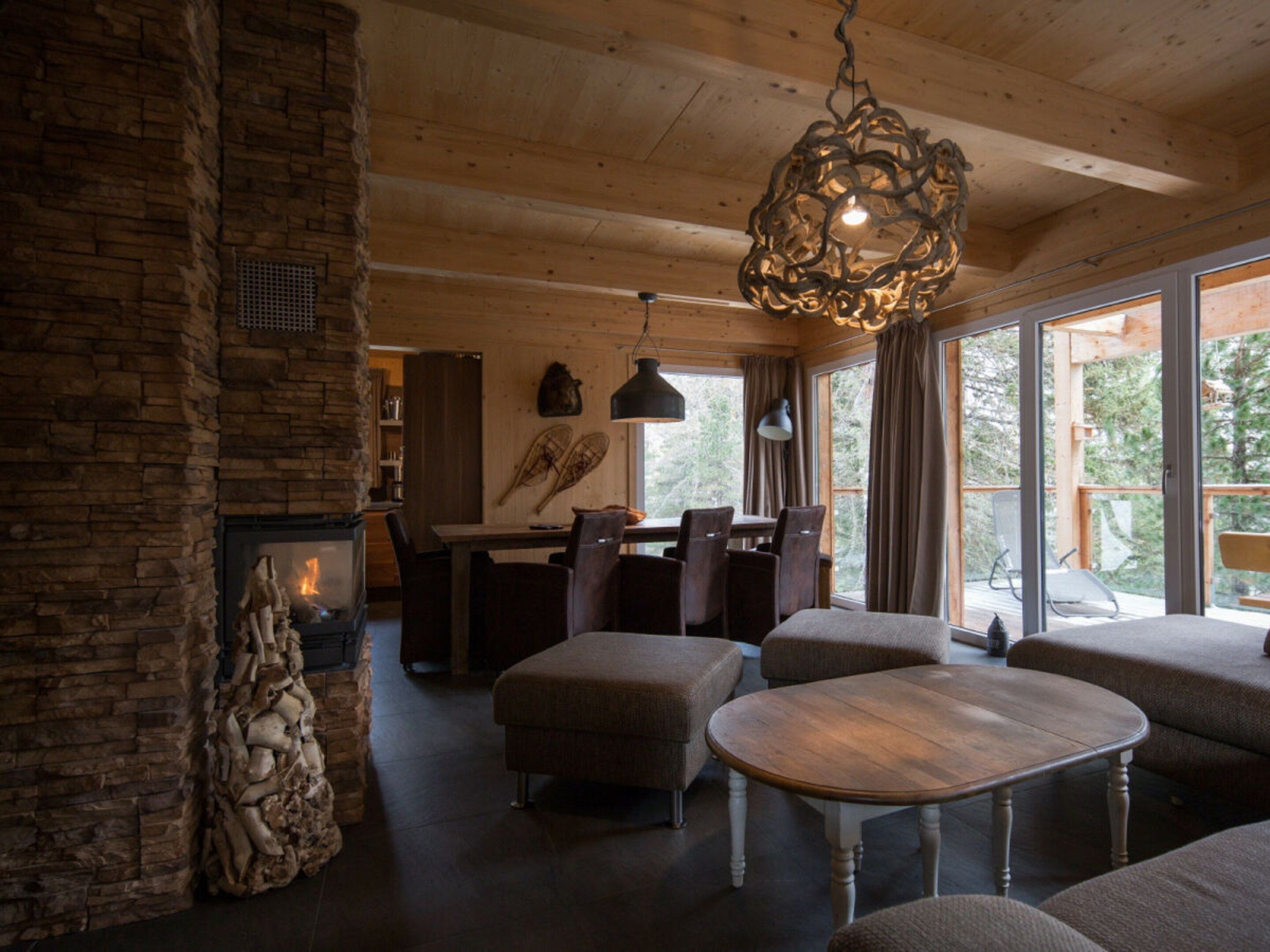 A cozy interior with a stone fireplace, wooden ceiling, and a dining area with chairs and a table.