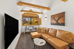 A modern living room with a large flat-screen TV, a leather sofa, a small coffee table, and a desk with a computer. - Sundancer Lodge - True Ski-In/Out+Hot Tub+Views (Mountain Village)
