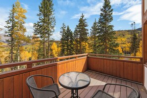 A wooden deck with two wicker chairs and a glass table, overlooking a forest with autumn foliage. - Sundancer Lodge - True Ski-In/Out+Hot Tub+Views (Mountain Village)
