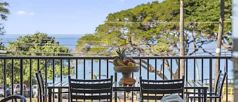 A balcony with a view of the sea, equipped with two chairs and a table with a fruit bowl.