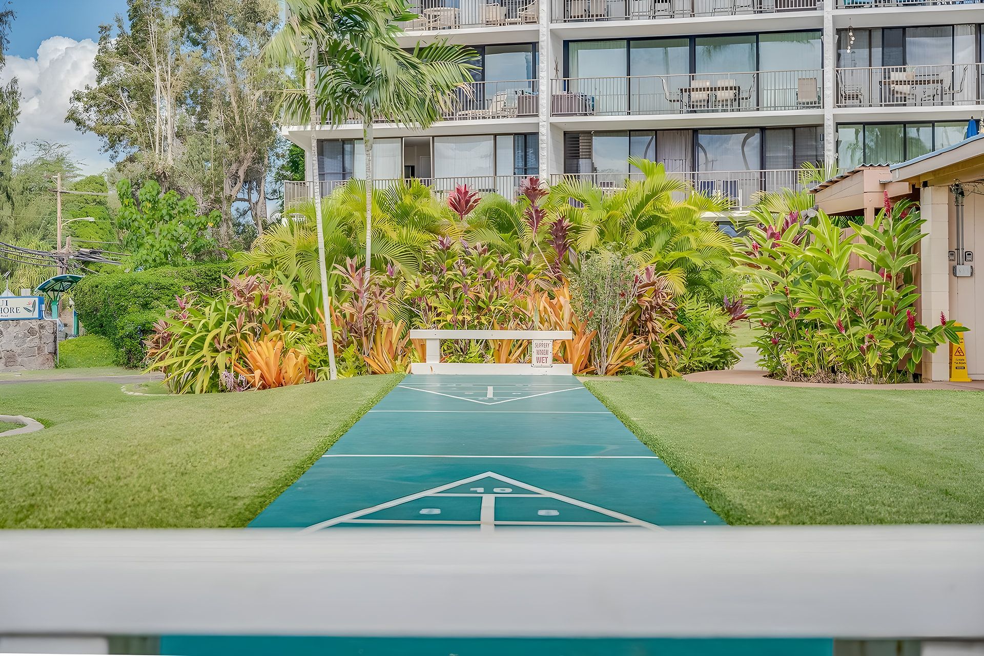 A hotel entrance with a green pathway leading to a white building with multiple balconies.