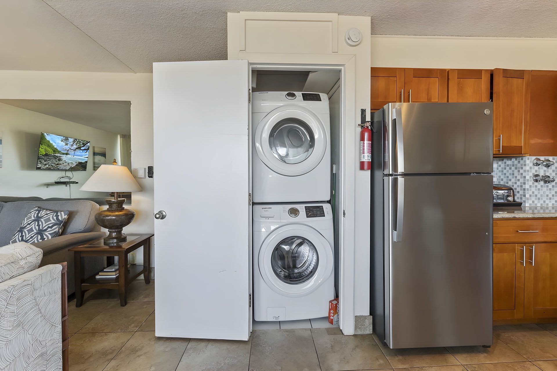 Cocina compacta con lavadora y secadora integradas, refrigerador de acero inoxidable y muebles de madera.