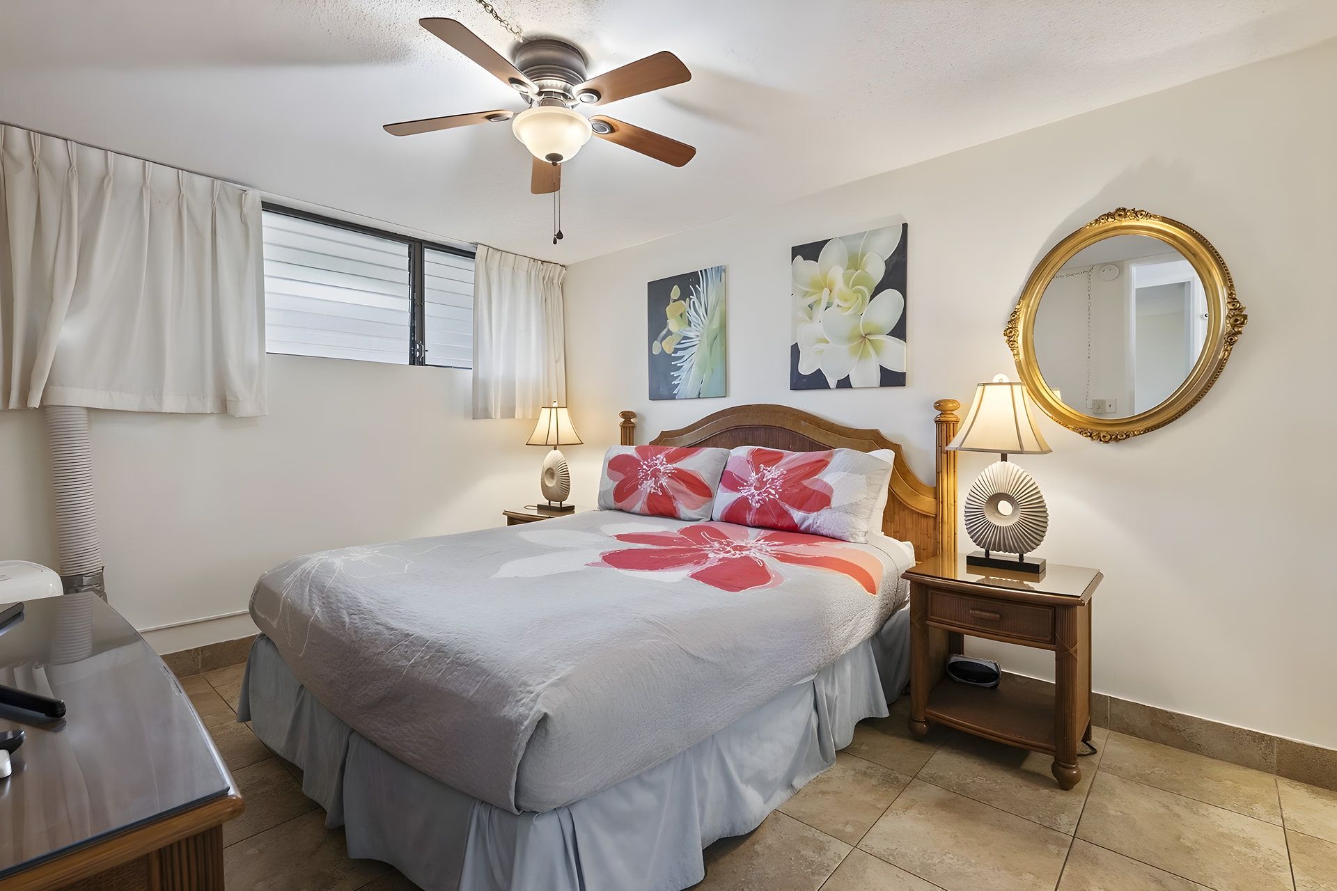 Une chambre d’hôtel avec un lit, deux lampes de chevet, un ventilateur de plafond, un grand miroir et des œuvres d’art accrochées aux murs.