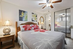 A bedroom with a bed, a nightstand, a lamp, a ceiling fan, and a mirror. - Kihei, Maui Parkshore, Spacious 4 BR, Sleeps 12 (Kihei)