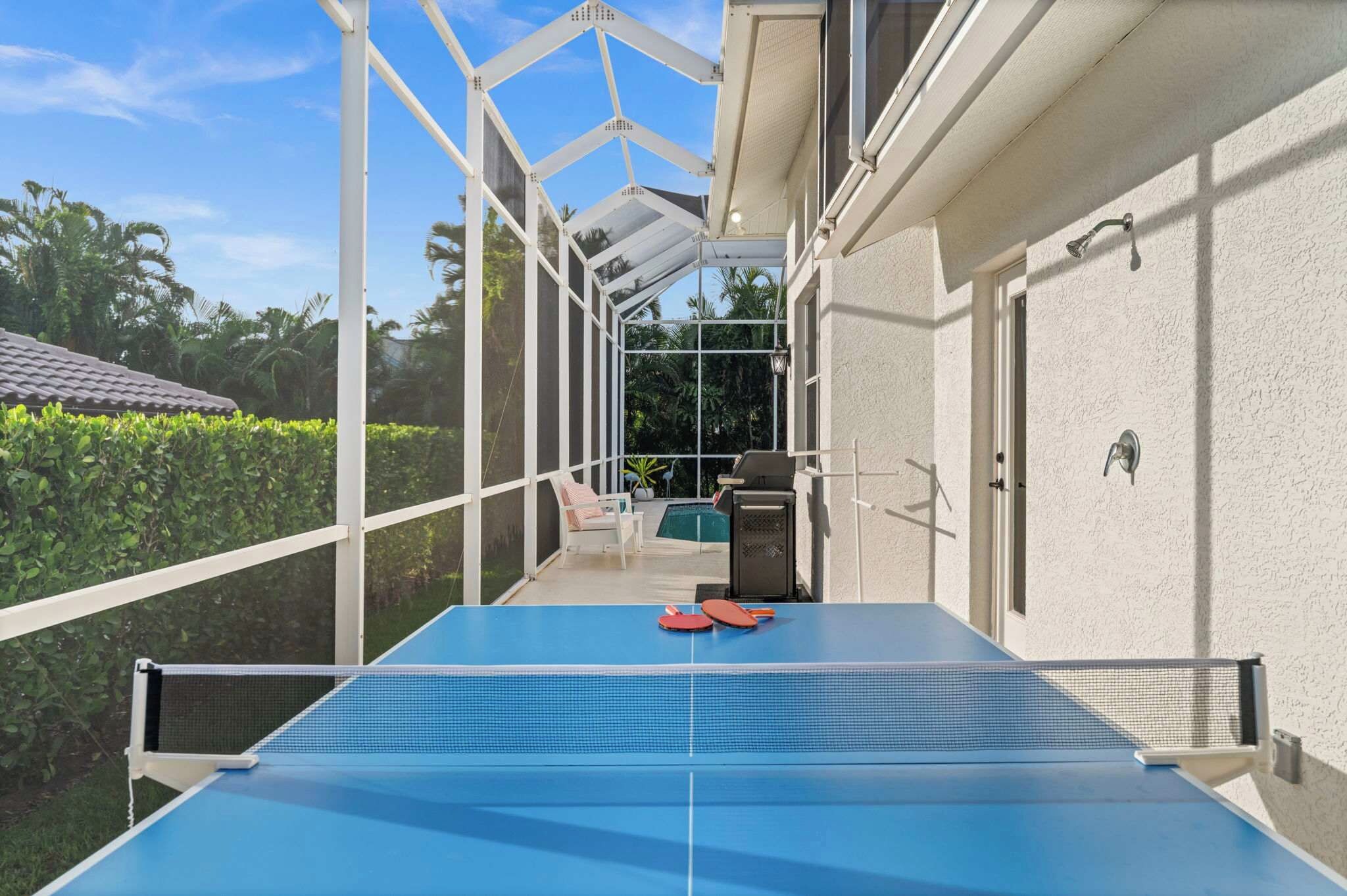 Et overdækket udendørs område med et bordtennisbord, grill og swimmingpool.