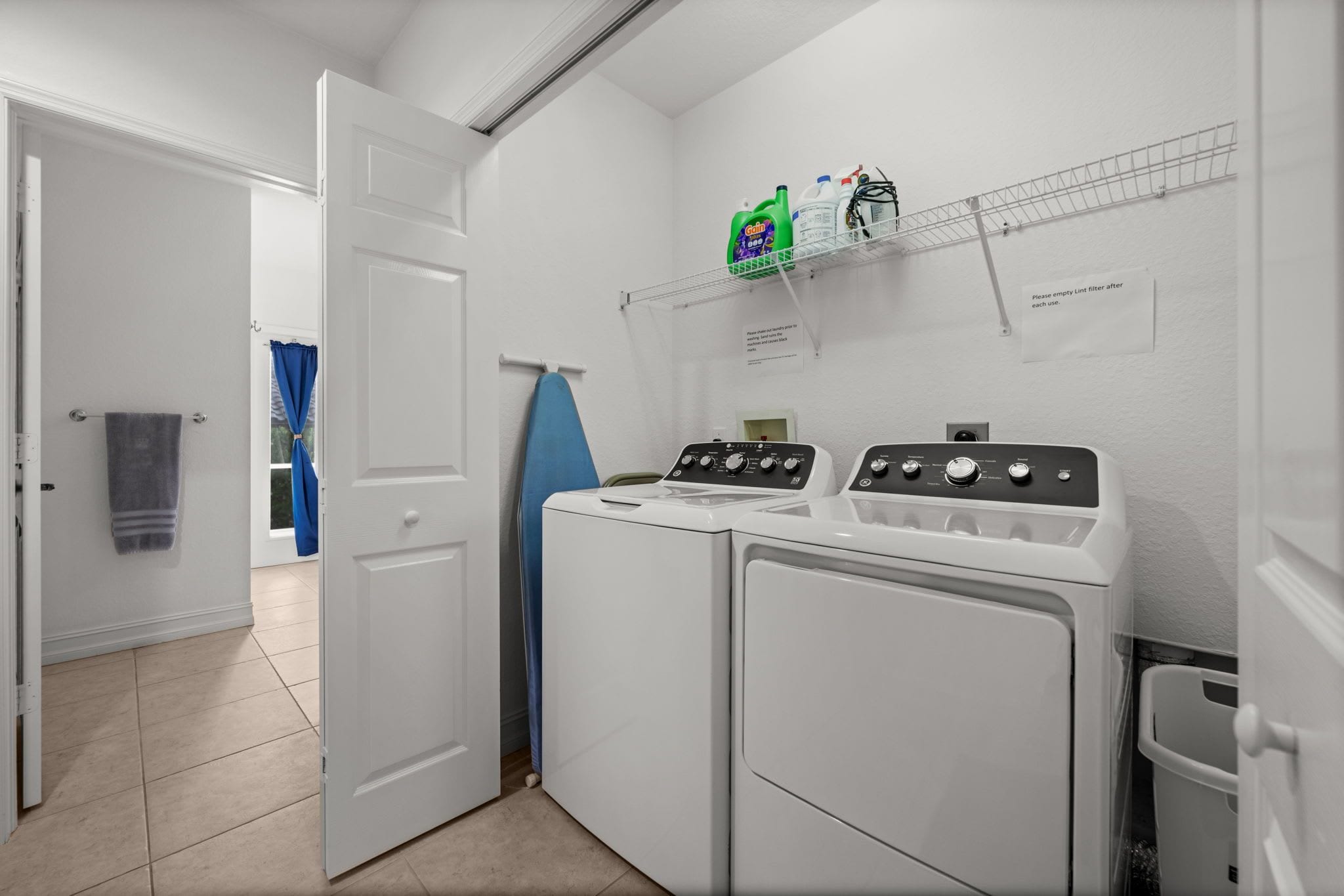 Une buanderie équipée d’un lave-linge et d’un sèche-linge à chargement frontal, d’une étagère contenant des produits de nettoyage et d’une porte donnant sur une autre pièce.