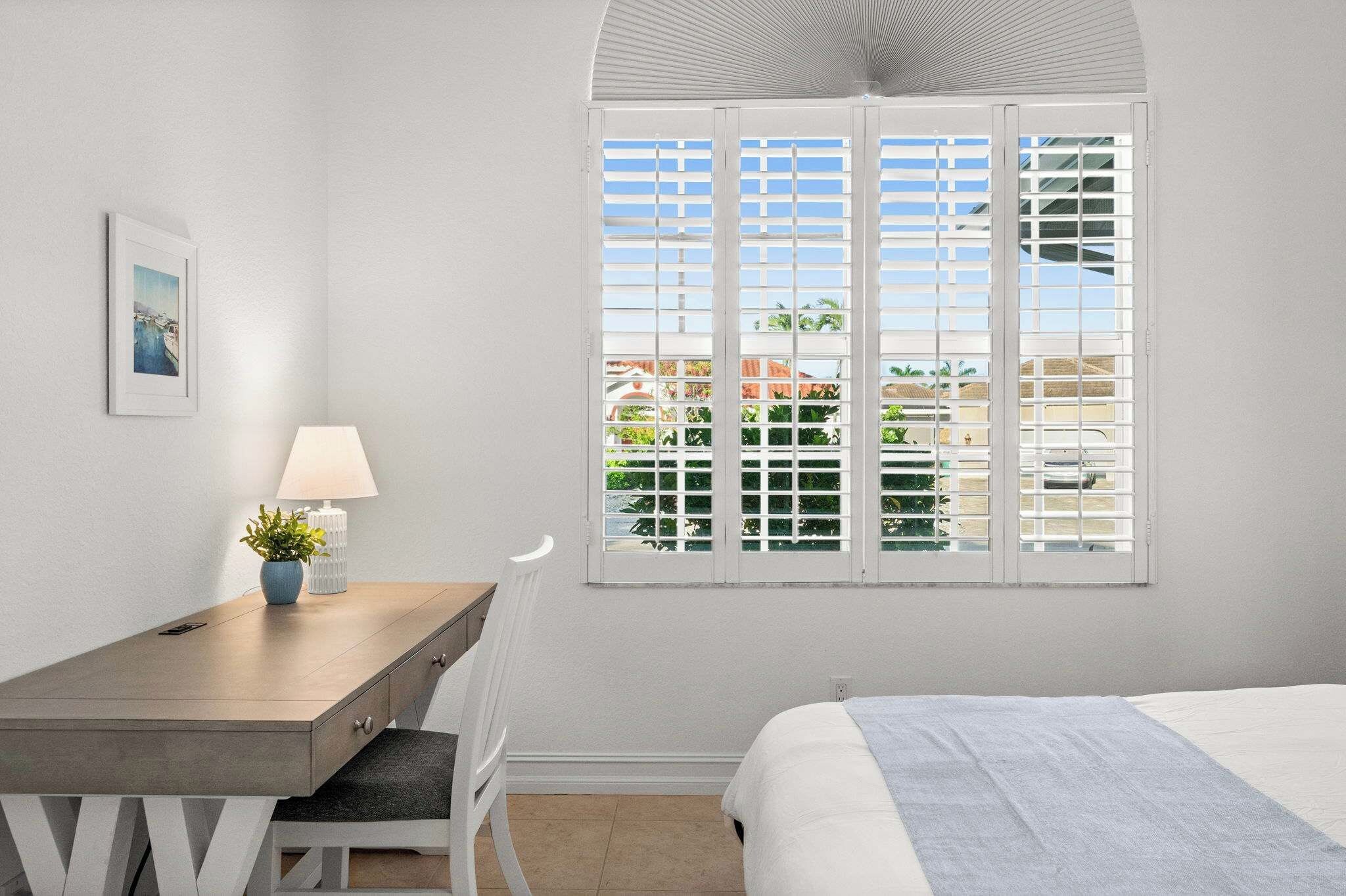 A hotel room with a bed, a desk with a lamp, a chair, and a window with a view of the outdoors.