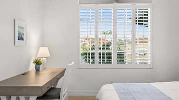 A hotel room with a bed, a desk with a lamp, a chair, and a window with a view of the outdoors.