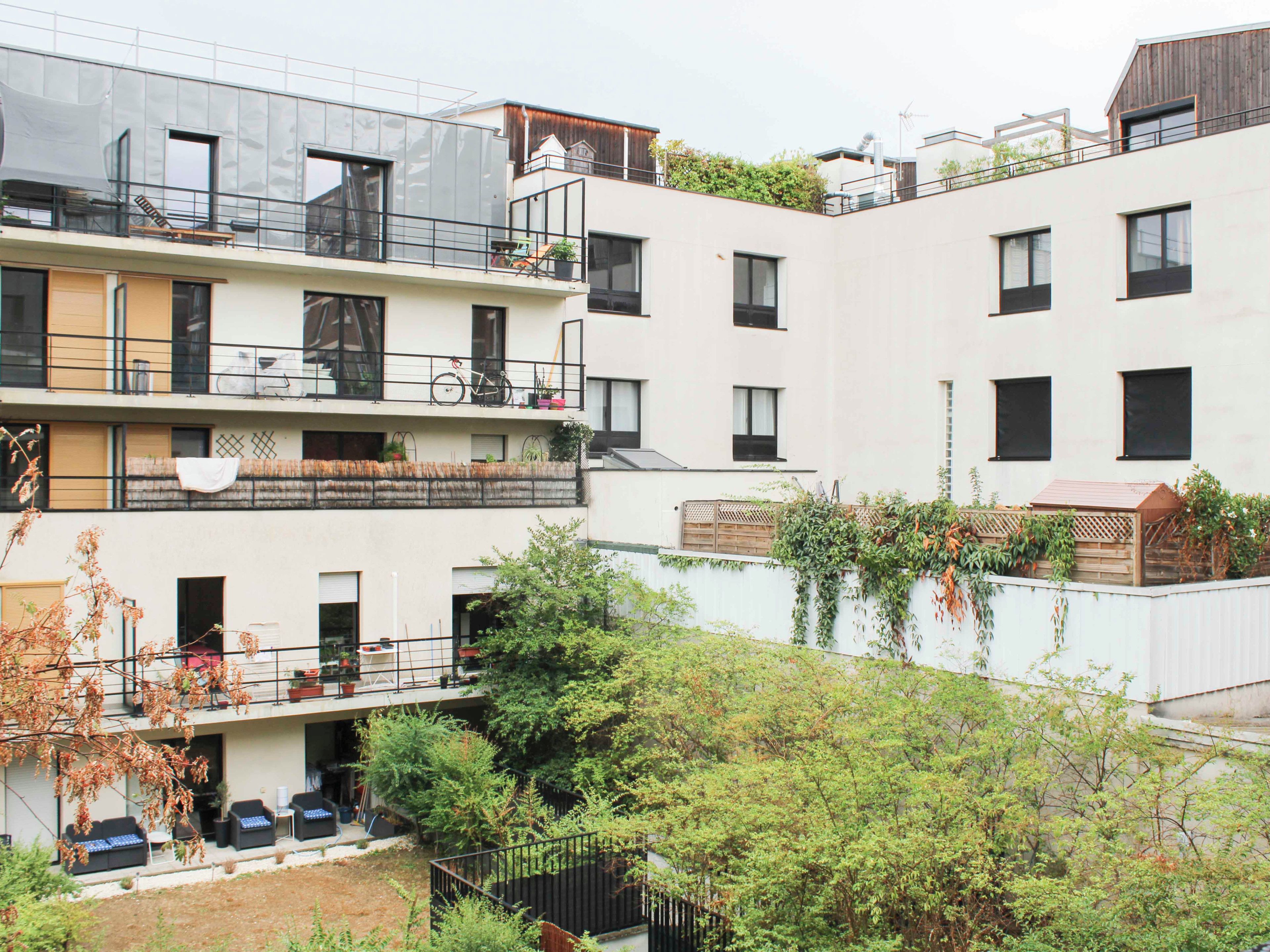 Un edificio residencial de varios pisos con balcones, mobiliario exterior y zonas verdes.