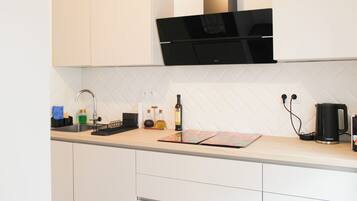 A modern kitchen with white cabinetry, a black range hood, a sink with a faucet, and a kettle on the countertop.