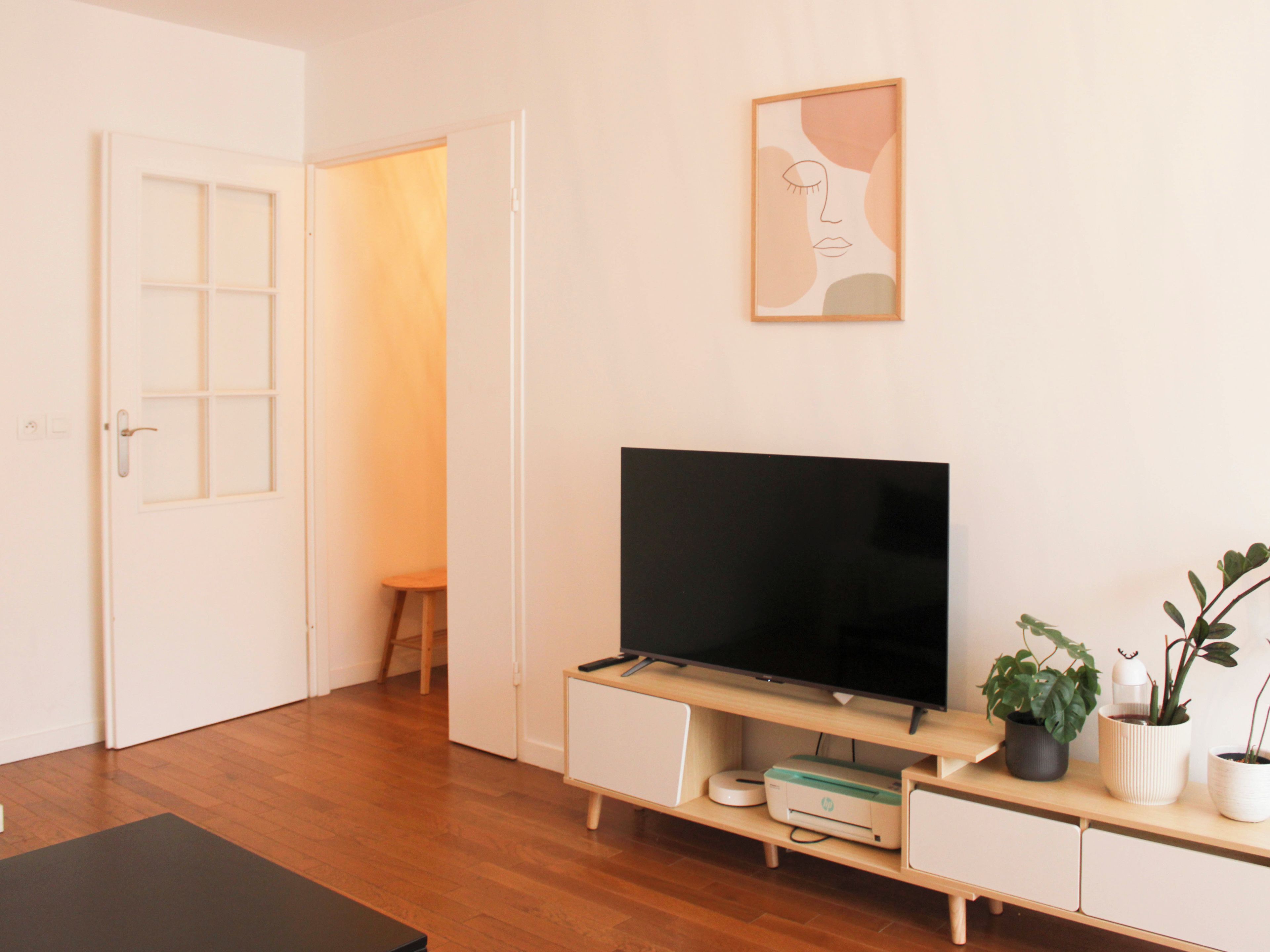 Une pièce avec un téléviseur posé sur un meuble, une porte, un petit tabouret et un tableau accroché au mur.