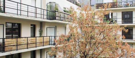 A multi-story residential building with balconies, a tree in the foreground, and a clear sky.
