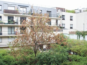 Un edificio residencial de varios pisos con balcones, un árbol en primer plano y una cerca blanca.
