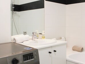 Un baño con lavamanos blanco, un espejo, cabina de ducha de vidrio y lavadora.