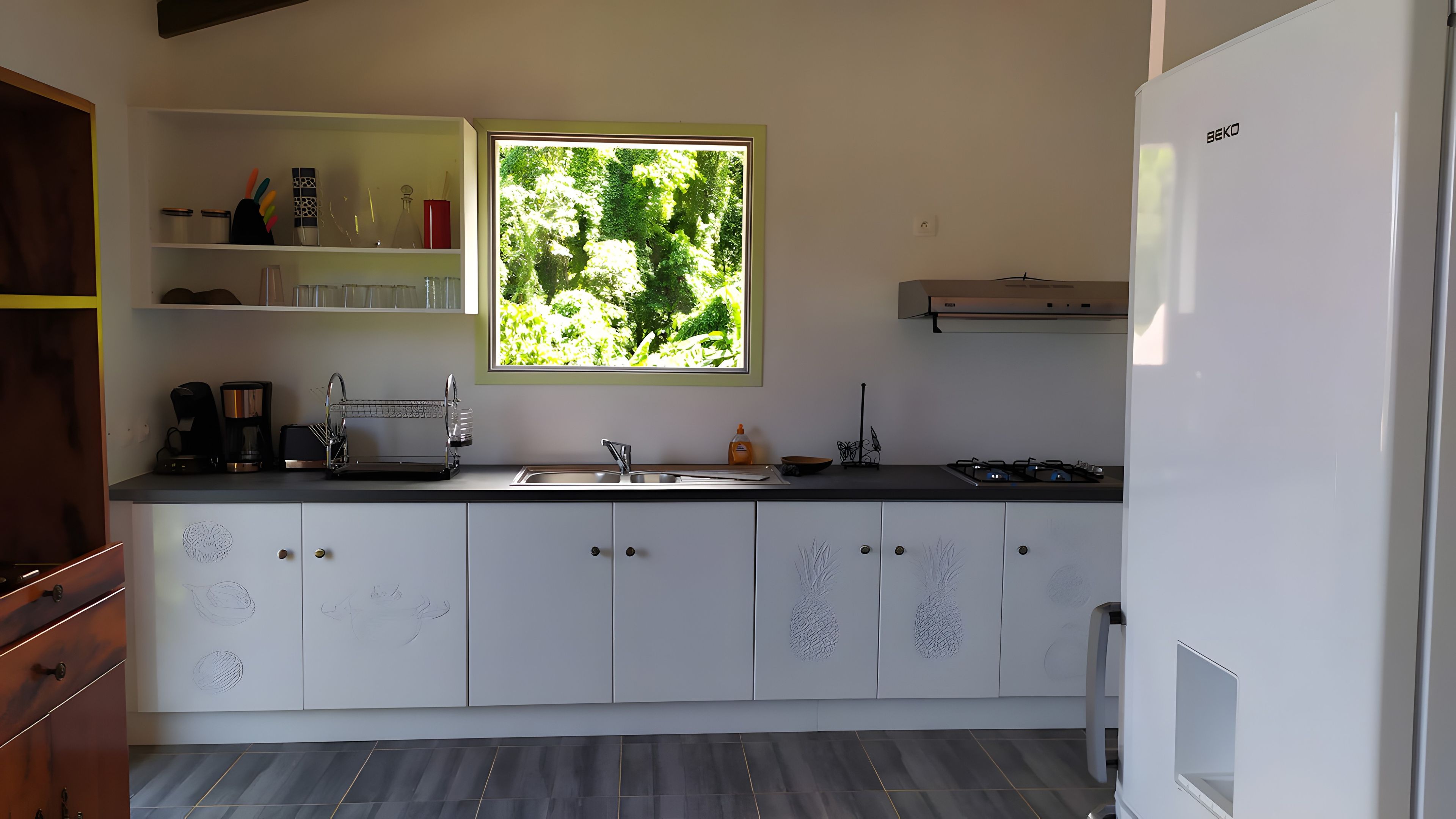 Een moderne keuken met witte kasten, een inbouwfornuis en een raam met uitzicht op groen.